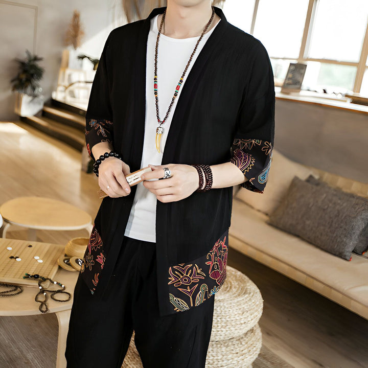 Homme portant un kimono noir brodé avec des motifs floraux colorés. Détail sur le col, les manches et le bas du kimono. Vêtements traditionnels japonais en vente.