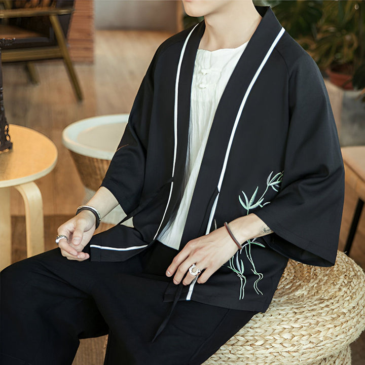 Homme portant un kimono noir avec des motifs de bambou, style japonais moderne. Vêtements traditionnels revisités. Idéal pour un look unique et élégant. Découvrez notre collection de kimonos.
