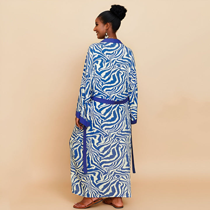 Femme portant un kimono long à motifs zébrés bleus et blancs, ceinture assortie. Vêtement élégant et confortable, idéal pour se détendre à la maison ou pour une occasion spéciale. Découvrez notre collection de kimonos uniques et tendance.