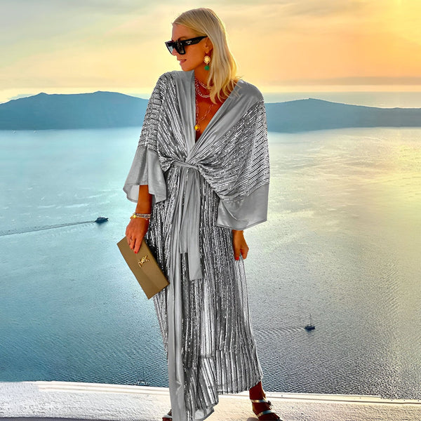 Femme élégante portant un kimono argenté scintillant, posant devant un paysage marin au coucher du soleil. Kimono long, ceinture nouée, manches amples. Mode kimono, vêtements d'été. Achetez notre collection de kimonos.