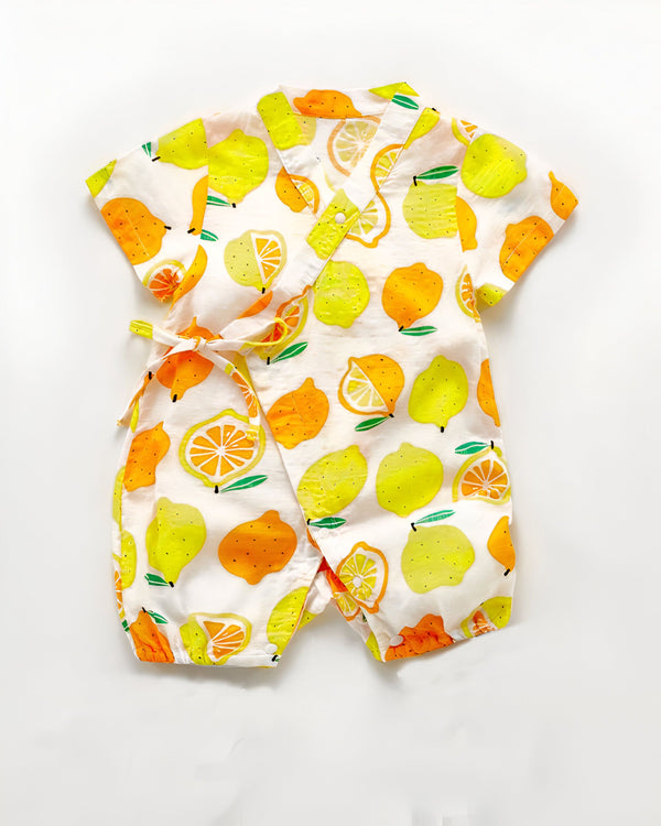 Barboteuse pour bébé à motifs d'agrumes (citrons et oranges) sur fond blanc. Combinaison légère à manches courtes et col croisé, idéale pour l'été. Vêtement confortable et mignon pour les tout-petits.