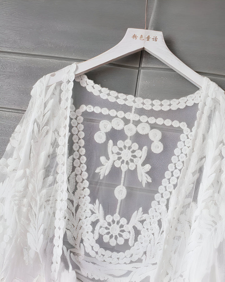 Kimono blanc en dentelle délicate suspendu sur un cintre. Vêtement léger et élégant, idéal pour compléter une tenue avec une touche bohème chic. Collection de kimonos en vente.