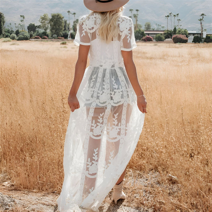 Femme portant un kimono blanc en dentelle, vue de dos, dans un champ doré. Kimono transparent avec motifs floraux, chapeau beige. Mode bohème, vente de kimonos en ligne.