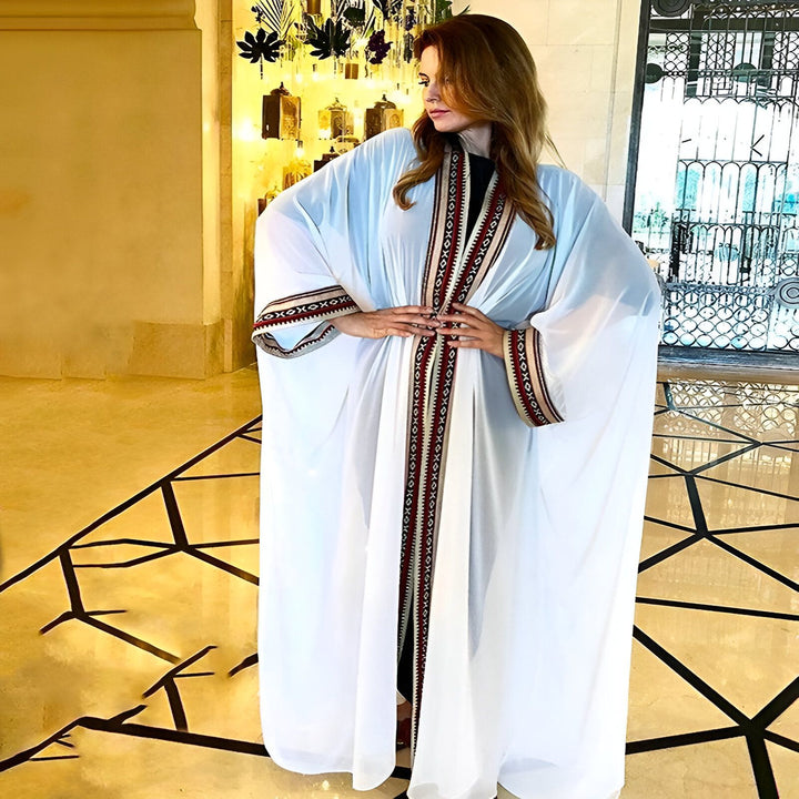 Femme portant un kimono blanc orné de motifs traditionnels rouges et beiges. Élégance et style dans notre collection de kimonos. Découvrez nos nouveautés!