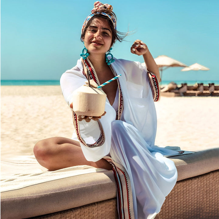 Femme souriante en kimono blanc sur la plage, tenant une noix de coco. Vêtements de plage élégants. Mode kimono pour l'été. Collection de kimonos de plage.