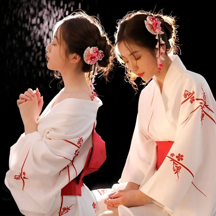 Deux femmes portant des kimonos blancs traditionnels ornés de motifs floraux rouges. Coiffure ornée de fleurs roses. Vente de kimonos.