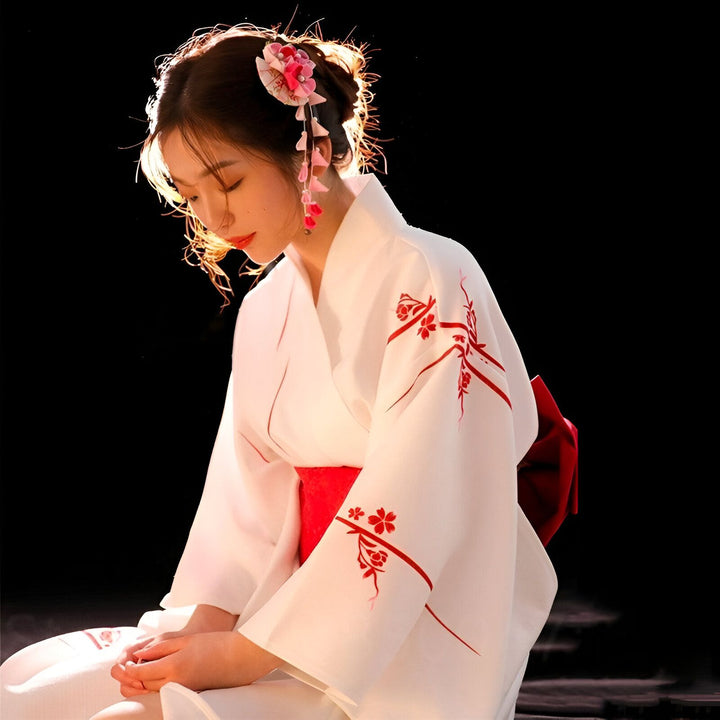 Femme portant un kimono blanc orné de motifs floraux rouges et une ceinture assortie. Coiffure ornée de fleurs. Boutique de kimonos en ligne.