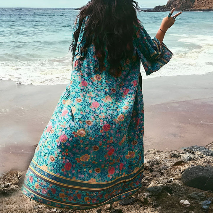 Femme portant un kimono fleuri sur une plage ensoleillée. Vêtements de plage et tenues d'été, style bohème. Découvrez notre collection de kimonos uniques.