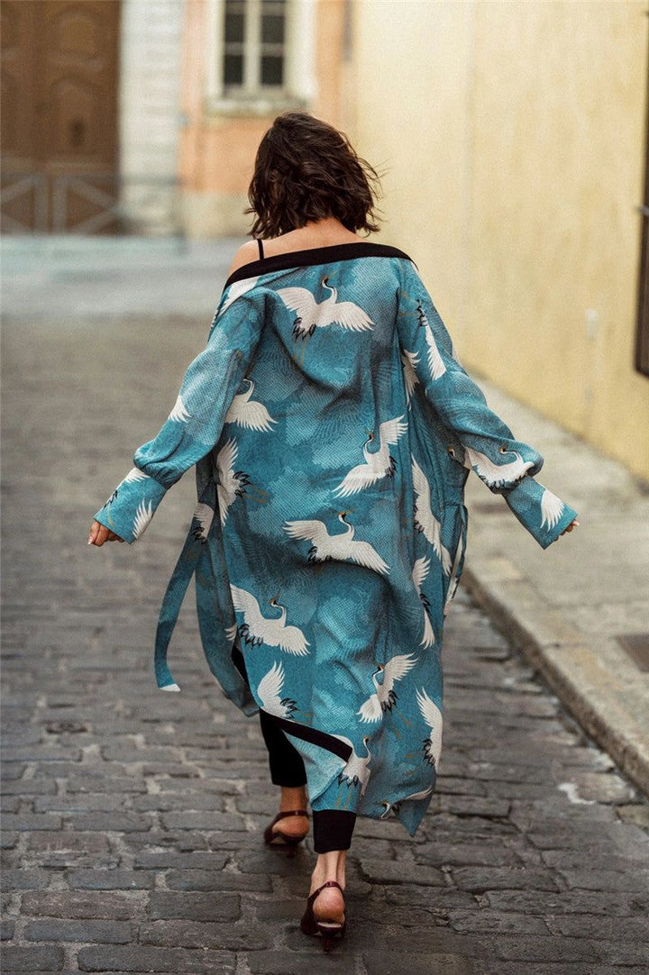 Femme de dos portant un kimono turquoise orné de motifs de grues blanches. Kimono long avec ceinture et manches amples. Style décontracté et élégant. Boutique de kimonos en ligne.