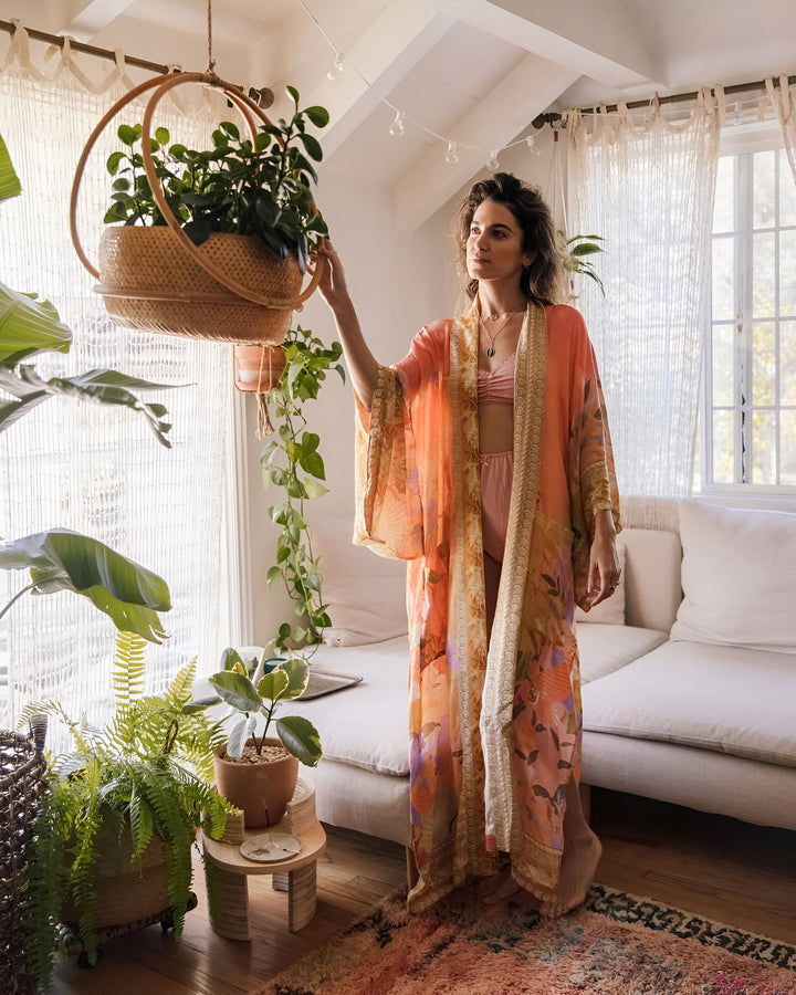 Femme portant un kimono coloré dans un intérieur lumineux et verdoyant. Kimono fleuri, vêtement d'intérieur tendance, style bohème. Découvrez notre collection de kimonos.