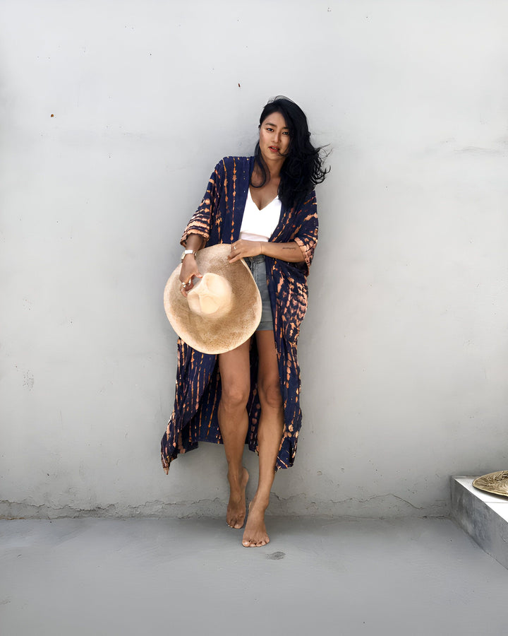 Femme portant un kimono long bleu et orange, short en jean et débardeur blanc, avec un chapeau de paille. Kimonos tendance à découvrir sur notre boutique en ligne.