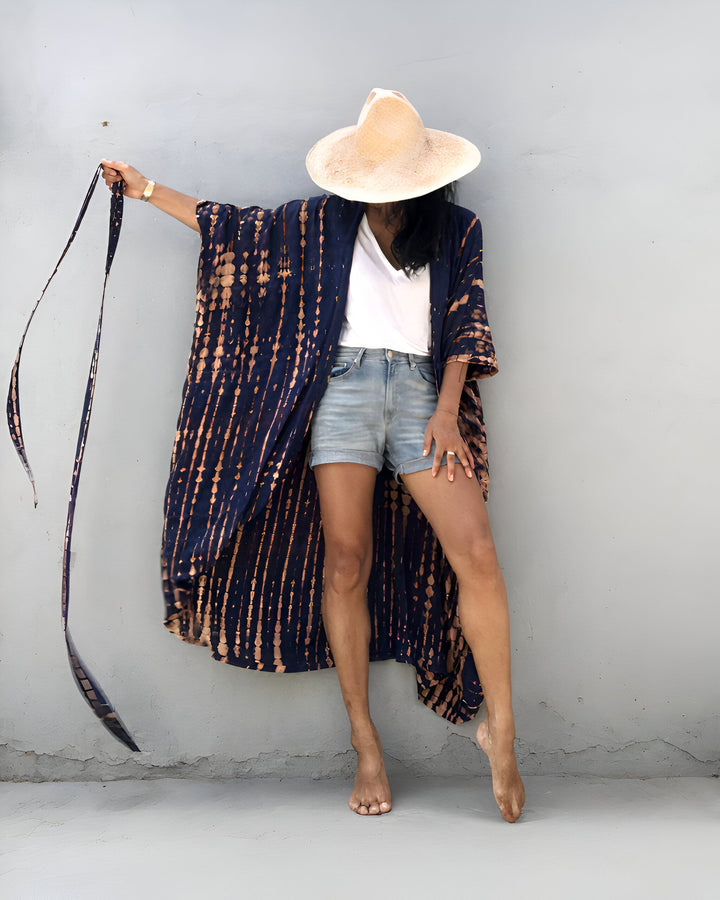 Femme portant un kimono bleu tie-dye avec un short en jean et un chapeau. Collection de kimonos chics et confortables pour toutes les occasions.