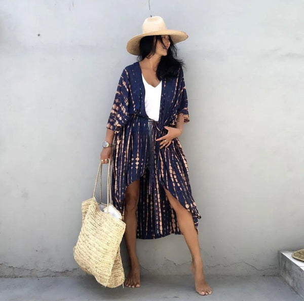 Femme portant un kimono tie-dye bleu et beige, chapeau de paille et sac en raphia. Vêtements de plage, style bohème. Boutique de kimonos en ligne.