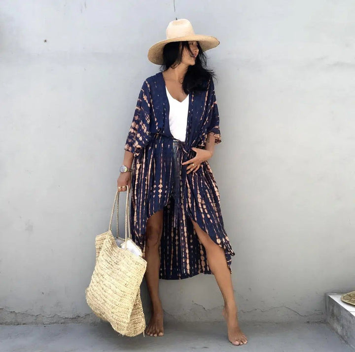 Femme portant un kimono tie-dye bleu et beige, chapeau de paille et sac en raphia. Vêtements de plage, style bohème. Boutique de kimonos en ligne.