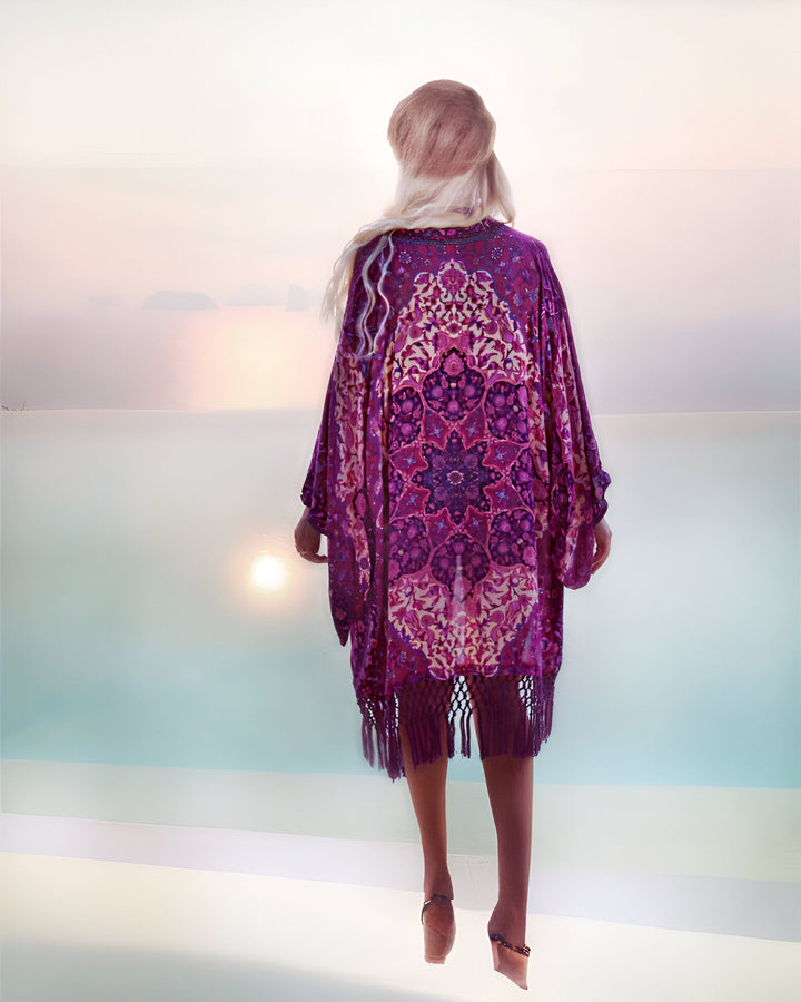 Femme portant un kimono violet à motifs complexes, regardant un coucher de soleil paisible sur l'océan. Vêtements de plage élégants. Kimonos à motifs uniques en vente.