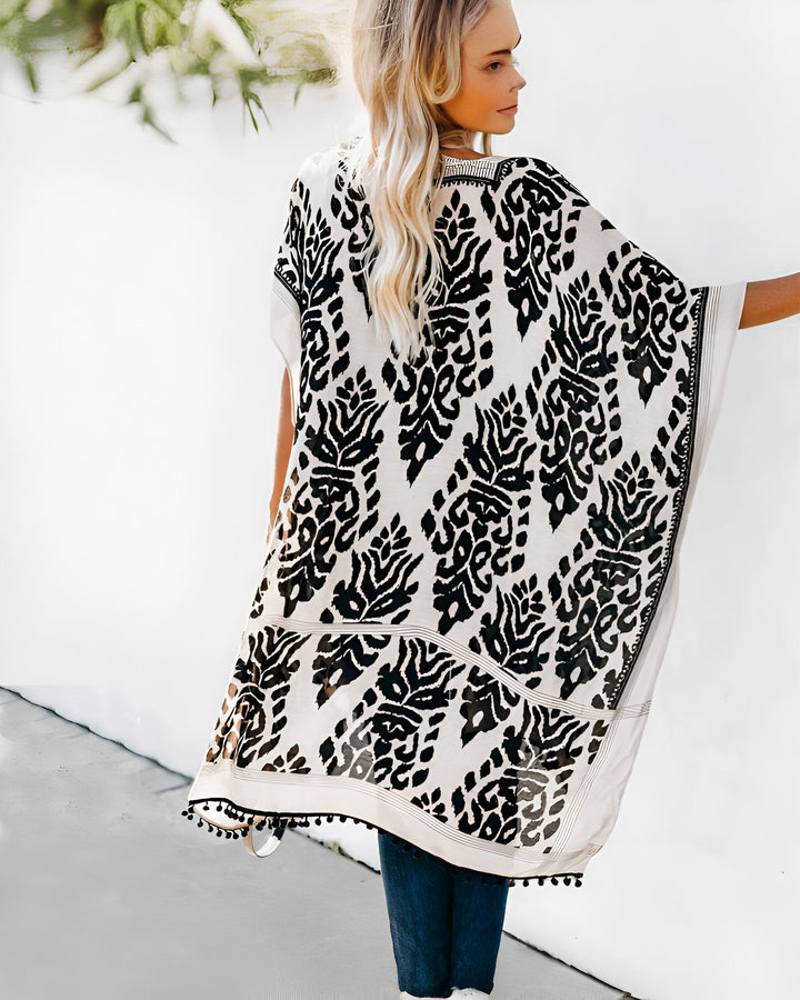 Femme blonde portant un kimono blanc à motifs noirs avec des pompons. Kimono léger et tendance idéal pour la boutique en ligne.