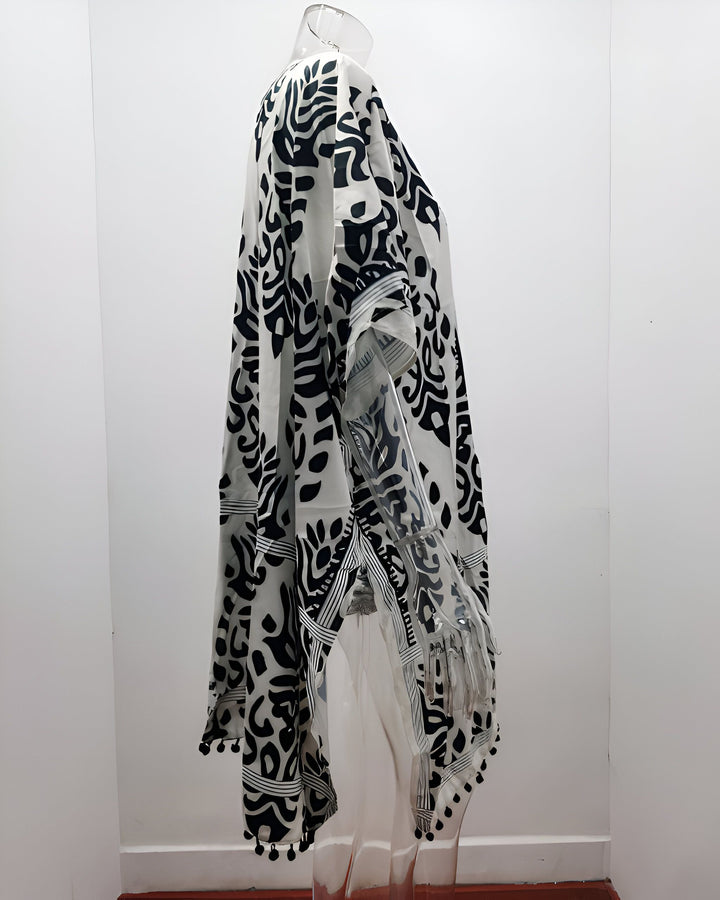 Kimono blanc et noir à motifs sur mannequin, style bohème avec pompons. Vêtement léger et confortable.