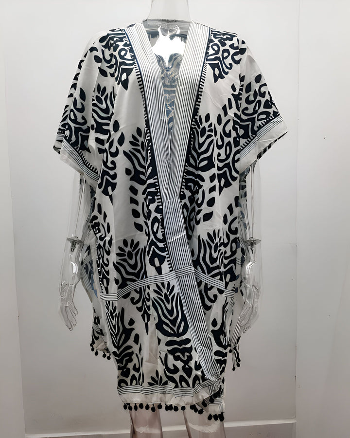 Kimono blanc à motifs noirs, idéal pour la plage ou la maison. Vêtement ample avec franges à pompons. Disponible dans notre collection de kimonos.