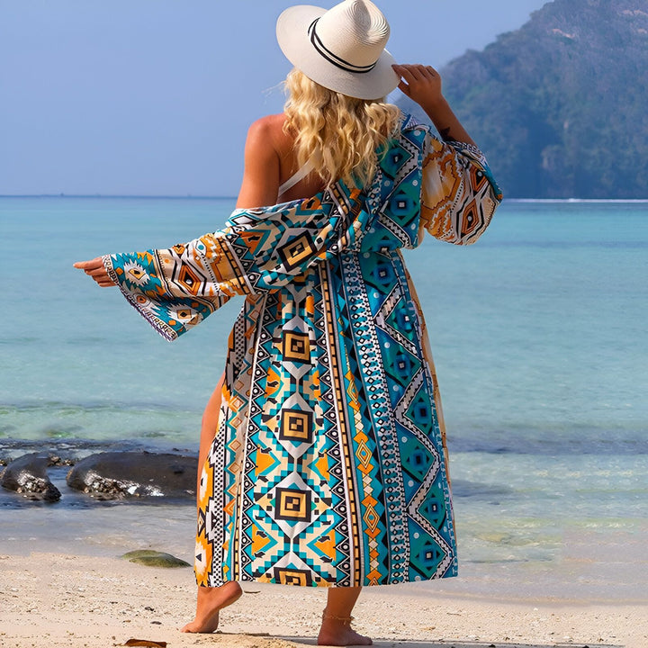Femme de dos portant un kimono coloré sur une plage de sable fin. Chapeau de paille et motif géométrique. Collection kimono tendance.