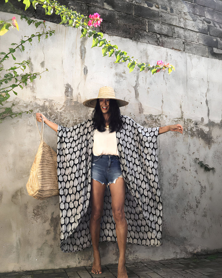 Femme souriante portant un kimono à motifs feuilles noir et blanc, un chapeau de paille et un sac tressé. Vente de kimonos élégants pour femmes.