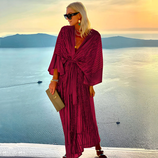 Femme portant un kimono bordeaux élégant avec ceinture, lunettes de soleil et pochette, sur fond de paysage marin. Vêtements kimono pour femmes disponibles à l'achat.