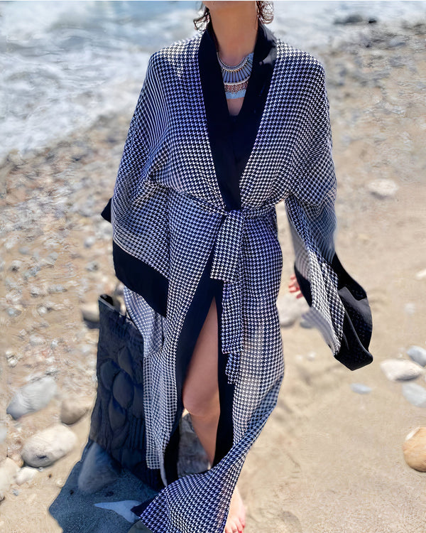 Femme portant un kimono long à motif pied-de-poule noir et blanc sur la plage. Vêtements de plage élégants et amples. Accessoires de mode, collier et sac. Kimono de plage de notre collection.