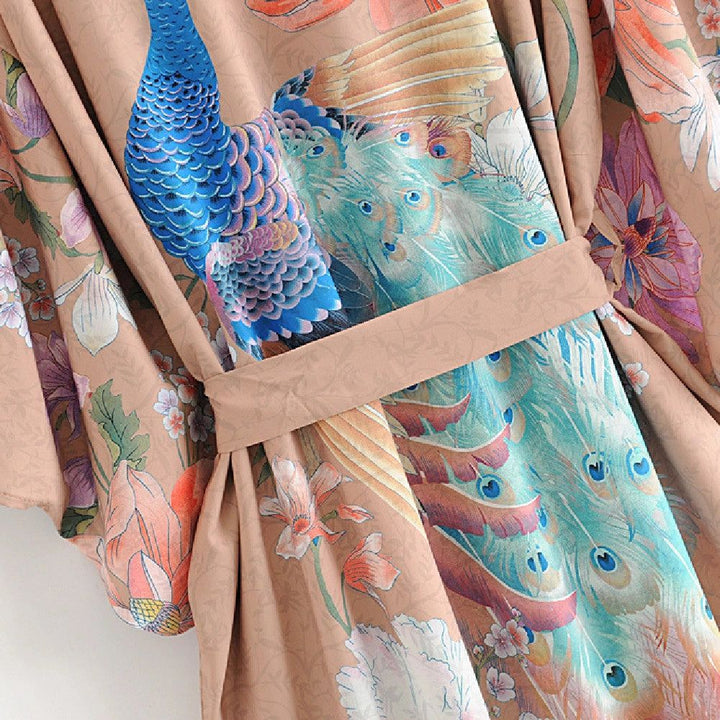Kimono beige orné de motifs de paons bleus et de fleurs colorées. Vêtement fluide et élégant pour femme. Collection de kimonos originaux.