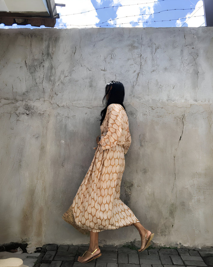 Femme portant un kimono beige à motifs, adossée à un mur texturé. Vente de kimonos élégants et confortables.