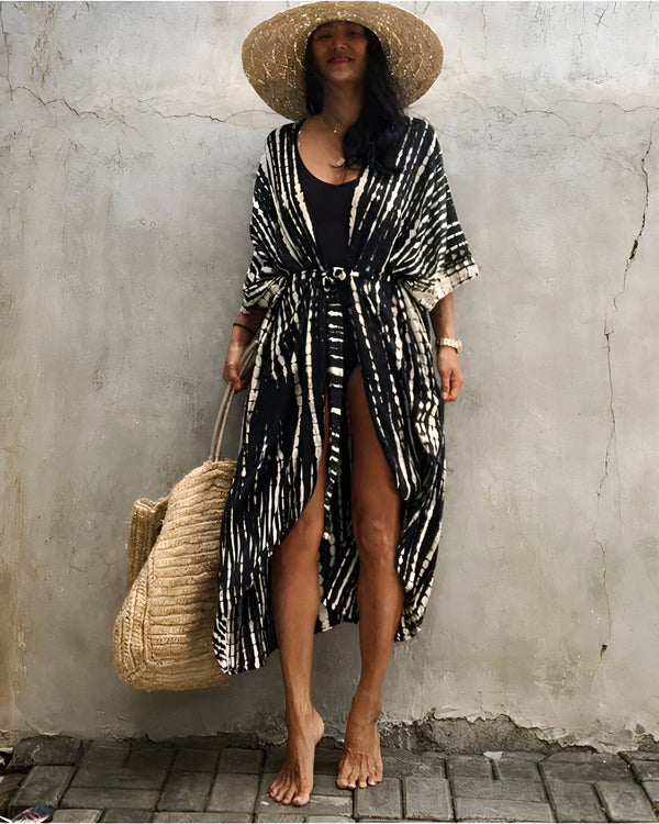 Femme portant un kimono noir et blanc à rayures, chapeau de paille et sac en osier. Idéal pour la plage ou une tenue décontractée. Découvrez notre collection de kimonos.