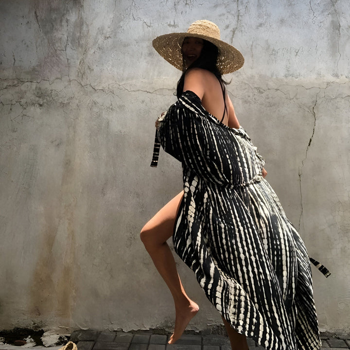 Femme souriante portant un kimono noir et blanc à rayures et un chapeau de paille. Vêtements de plage élégants. Collection de kimonos. Mode féminine estivale.