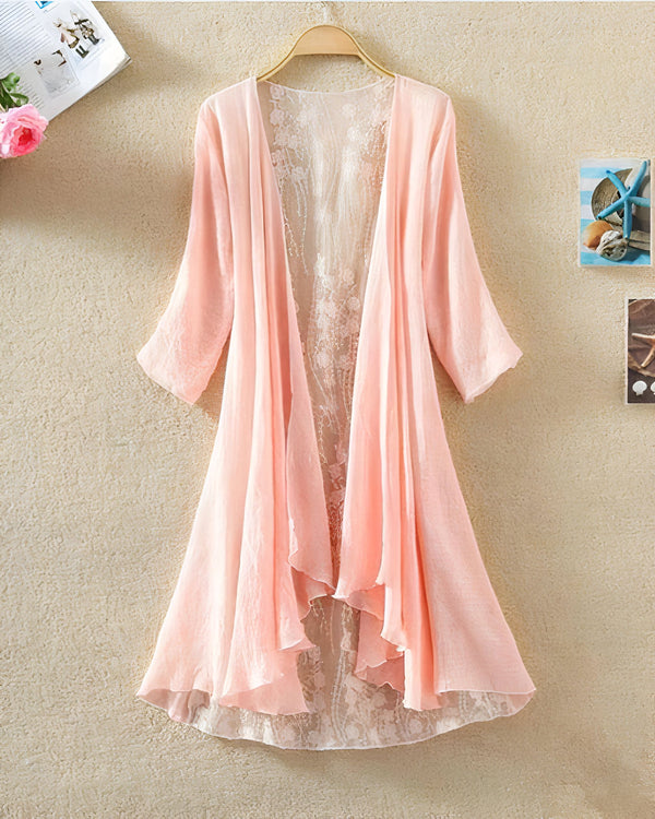 Kimono rose clair avec détails en dentelle florale, suspendu à un cintre. Vêtement léger et élégant, idéal pour la superposition. Découvrez notre collection de kimonos uniques.