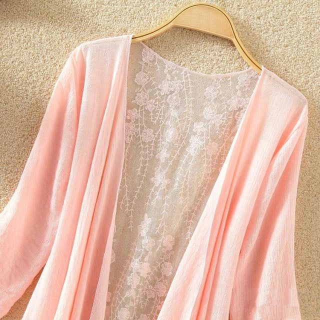 Kimono rose pâle avec dos en dentelle florale délicate, suspendu sur un cintre. Vêtement léger et élégant, parfait pour compléter votre look.