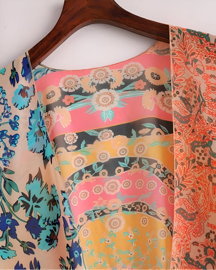 Kimono fleuri sur cintre. Motifs floraux variés : fleurs bleues, motifs orange et fleurs stylisées roses, jaunes et noires. Vêtement léger et coloré, idéal pour la boutique de kimonos.