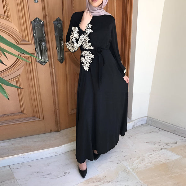 Kimono noir long avec broderies florales blanches, porté avec un hijab. Élégance et style oriental. Découvrez notre collection de kimonos uniques.