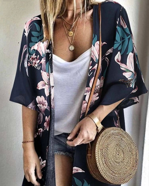 Kimono femme fleuri marine et rose porté sur un débardeur blanc et un short en jean. Un sac rond en osier complète le look. Découvrez nos kimonos pour un style unique.
