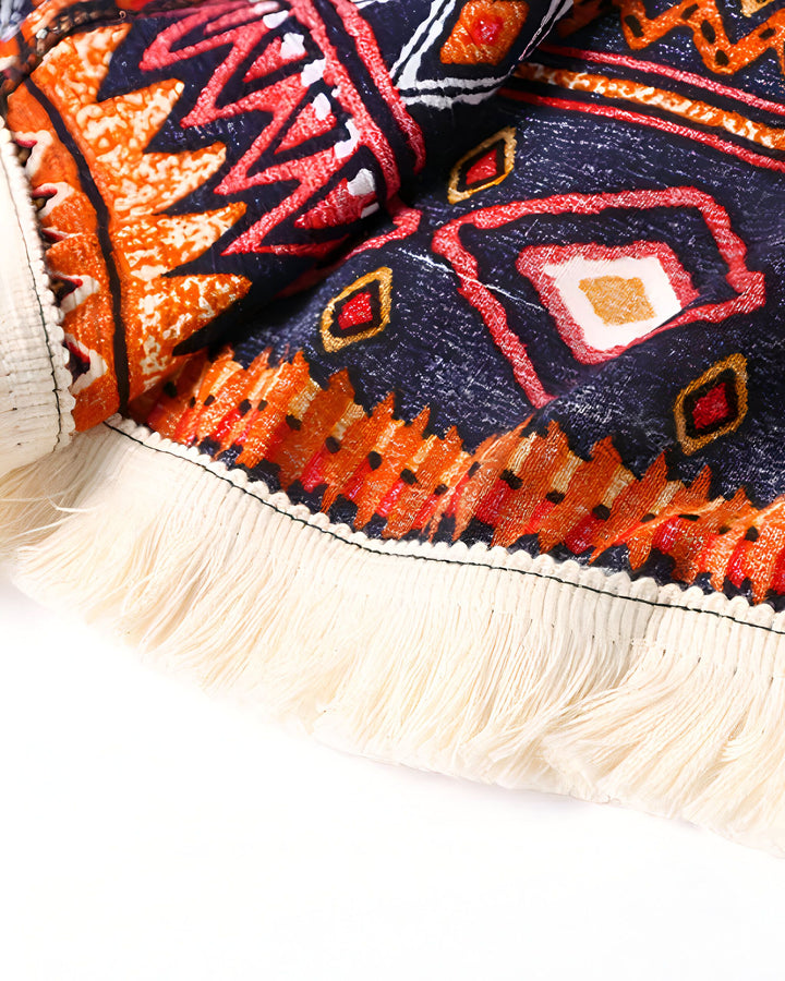 Détail texturé d'un kimono avec motifs ethniques orange, rouge et bleu marine. Franges blanches. Mode kimono, style bohème.