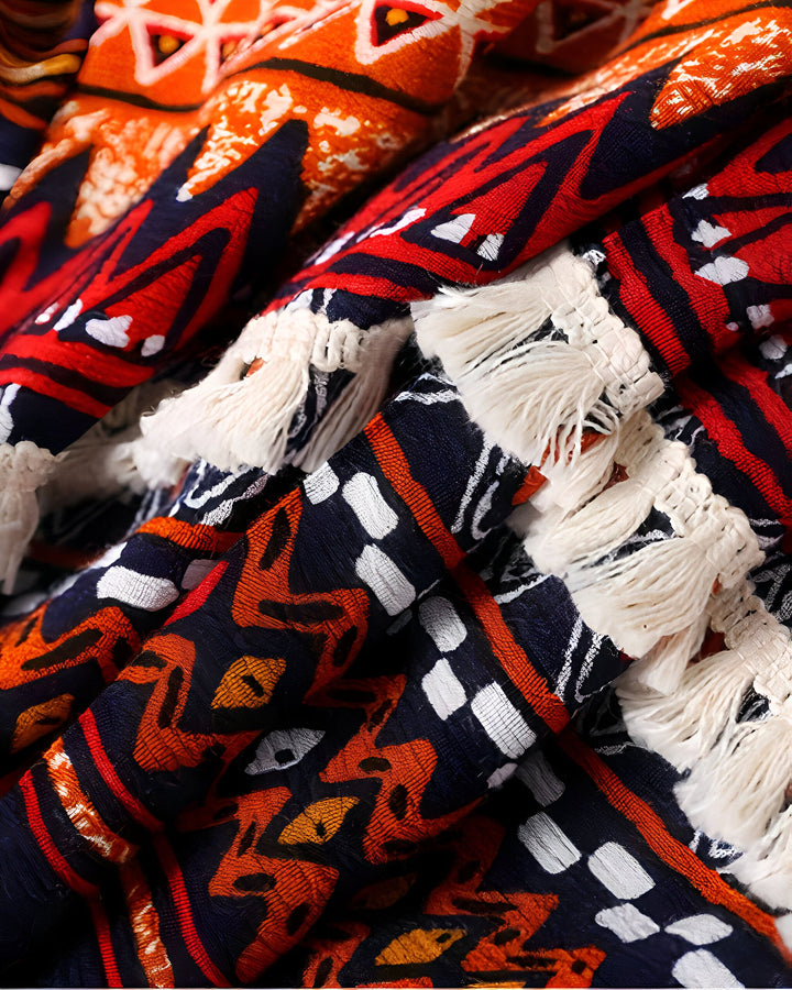 Détail d'un tissu de kimono avec motifs ethniques rouge, orange, marine. Franges décoratives blanches. Idéal pour un style unique et original.