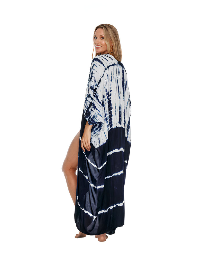 Femme blonde souriante portant une longue robe de plage tie-dye bleue et blanche. Elle regarde par-dessus son épaule. Vêtement d'été, style décontracté, vacances à la plage.