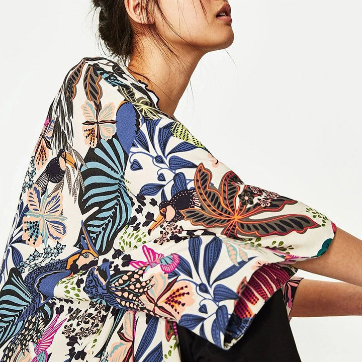 Femme portant un kimono à motifs tropicaux colorés avec des fleurs, des feuilles et des oiseaux. Style bohème, mode printemps-été.