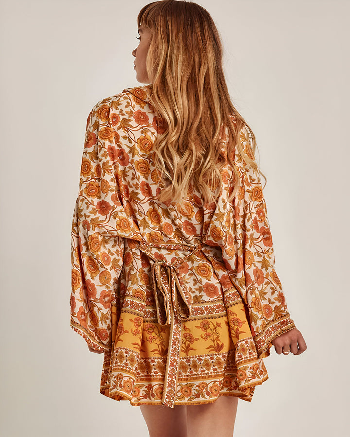 Femme portant un kimono court à motifs floraux orange et jaunes. Vue de dos, ceinture nouée à la taille. Vêtements de style kimono.