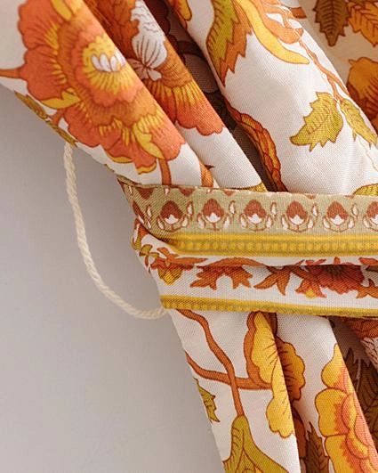 Détail d'un kimono avec motif floral orange et jaune. Texture du tissu. Ceinture assortie. Kimono pour femme, vêtement japonais revisité. Élégance et confort.