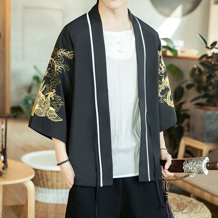 Homme portant un kimono noir avec broderies dorées de dragons sur les manches. Le kimono a des bordures blanches et est porté ouvert sur une chemise blanche à boutons.