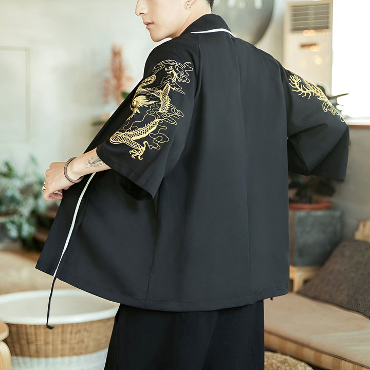 Homme portant un kimono noir avec des broderies de dragons dorés sur les manches. Vêtement de style japonais moderne avec une touche traditionnelle.