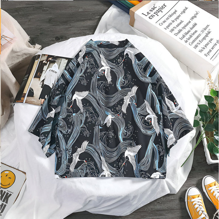 Kimono noir à motifs de grues blanches et d'ondulations sur un drap blanc. On aperçoit un magazine, une boîte à sourire, un sac en papier kraft, des baskets jaunes et une plante. Style asiatique.