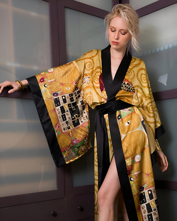 Femme blonde portant un kimono doré et noir avec des motifs inspirés de Klimt. Le kimono est fendu sur le côté et a une ceinture noire. Elle a des bracelets dorés.