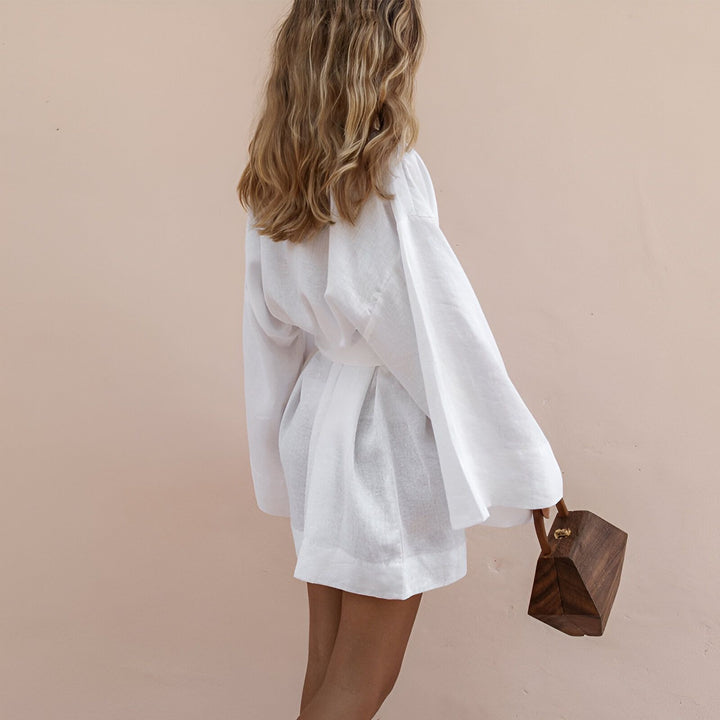 Femme portant un kimono blanc en lin avec une ceinture assortie, vue de dos, tenant un sac à main en bois. Kimono élégant et confortable à découvrir sur notre boutique en ligne.