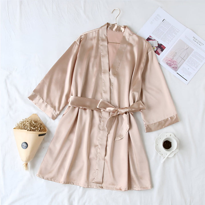 Kimono en soie champagne avec ceinture, suspendu sur un cintre. Fleurs séchées, magazine et tasse à café à proximité. Parfait pour se détendre avec style. Découvrez notre collection de kimonos en ligne.