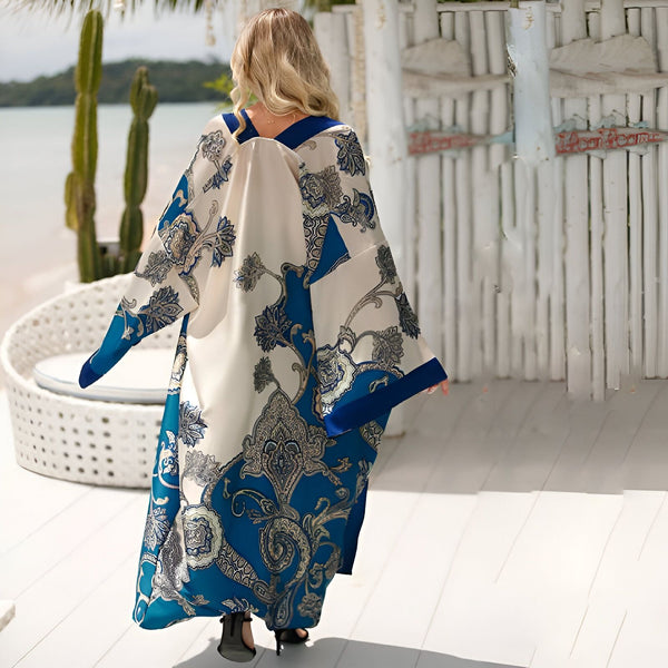 Femme de dos, portant une longue robe kimono blanche et bleue à motifs floraux sur une terrasse en bois avec vue sur la plage et la mer.