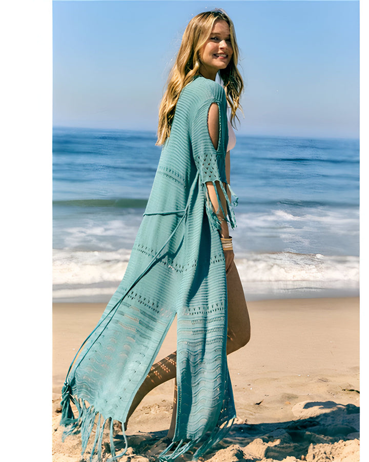 Femme souriante portant un kimono turquoise à franges sur la plage. Achetez nos kimonos en ligne. Vêtements de plage élégants et confortables. Idéal pour l'été et les vacances.