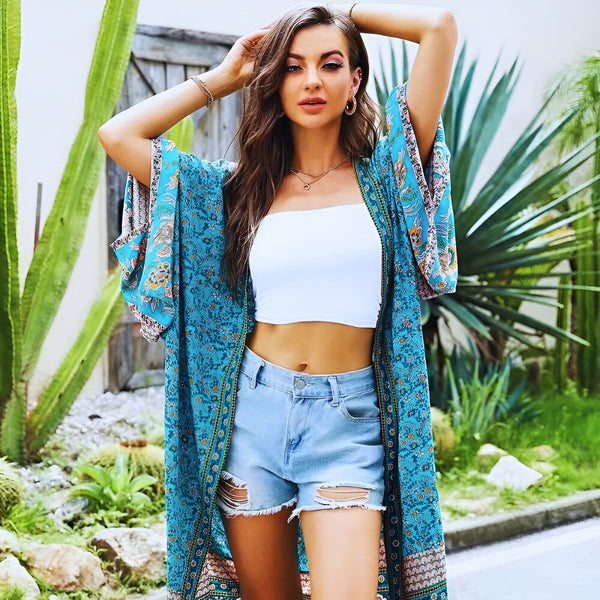 Femme portant un kimono bleu à motifs floraux, crop top blanc et short en jean. Vente de kimonos en ligne. Mode estivale, style bohème. Kimono long et léger, idéal pour l'été. Découvrez notre collection de kimonos.
